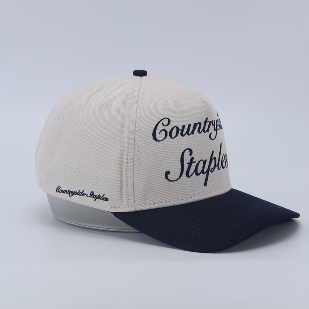 Signature Navy & Cream Countryside Staples Hat with embroidered logo laid flat on a white background side view.